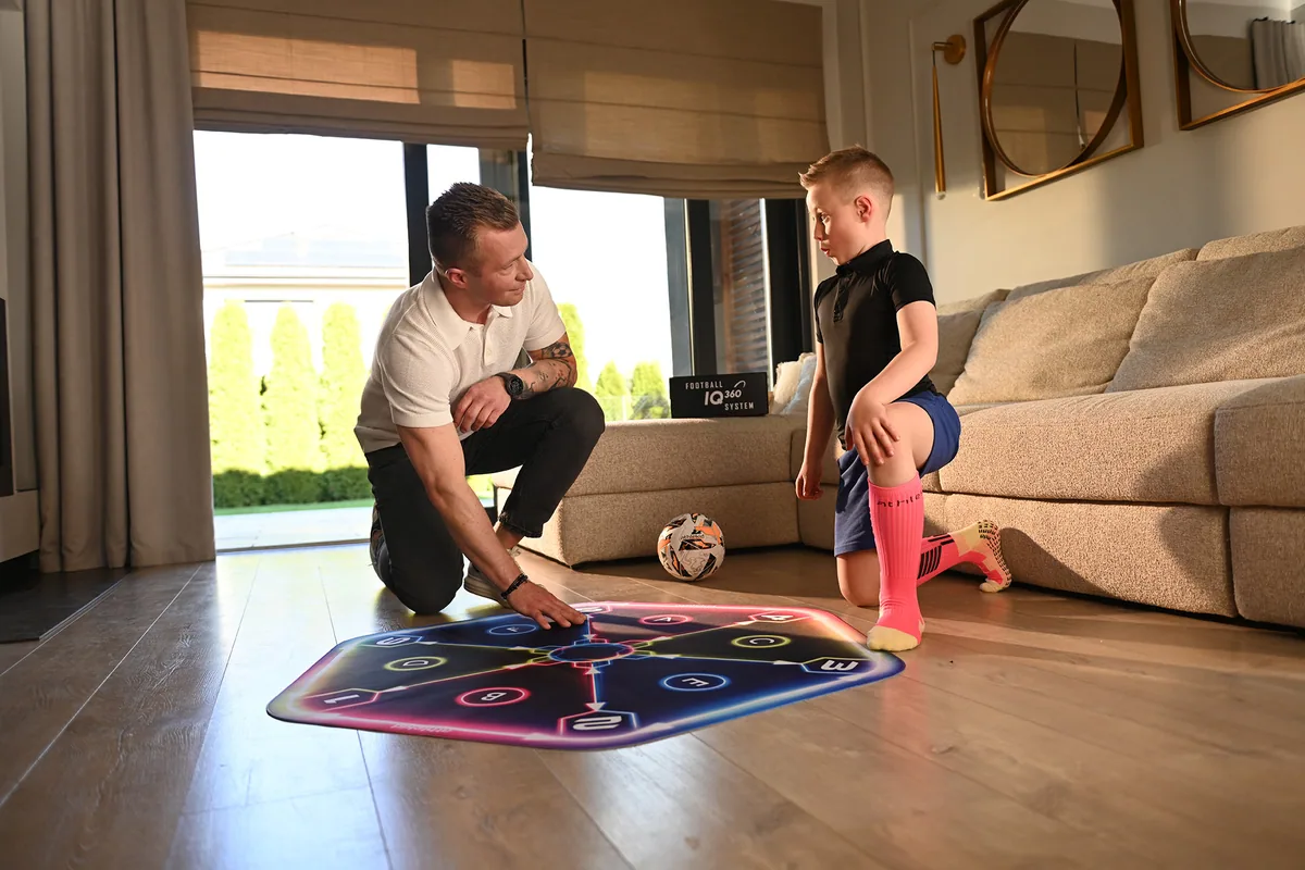 A parent kneeling beside the mat, showing his son an exercise